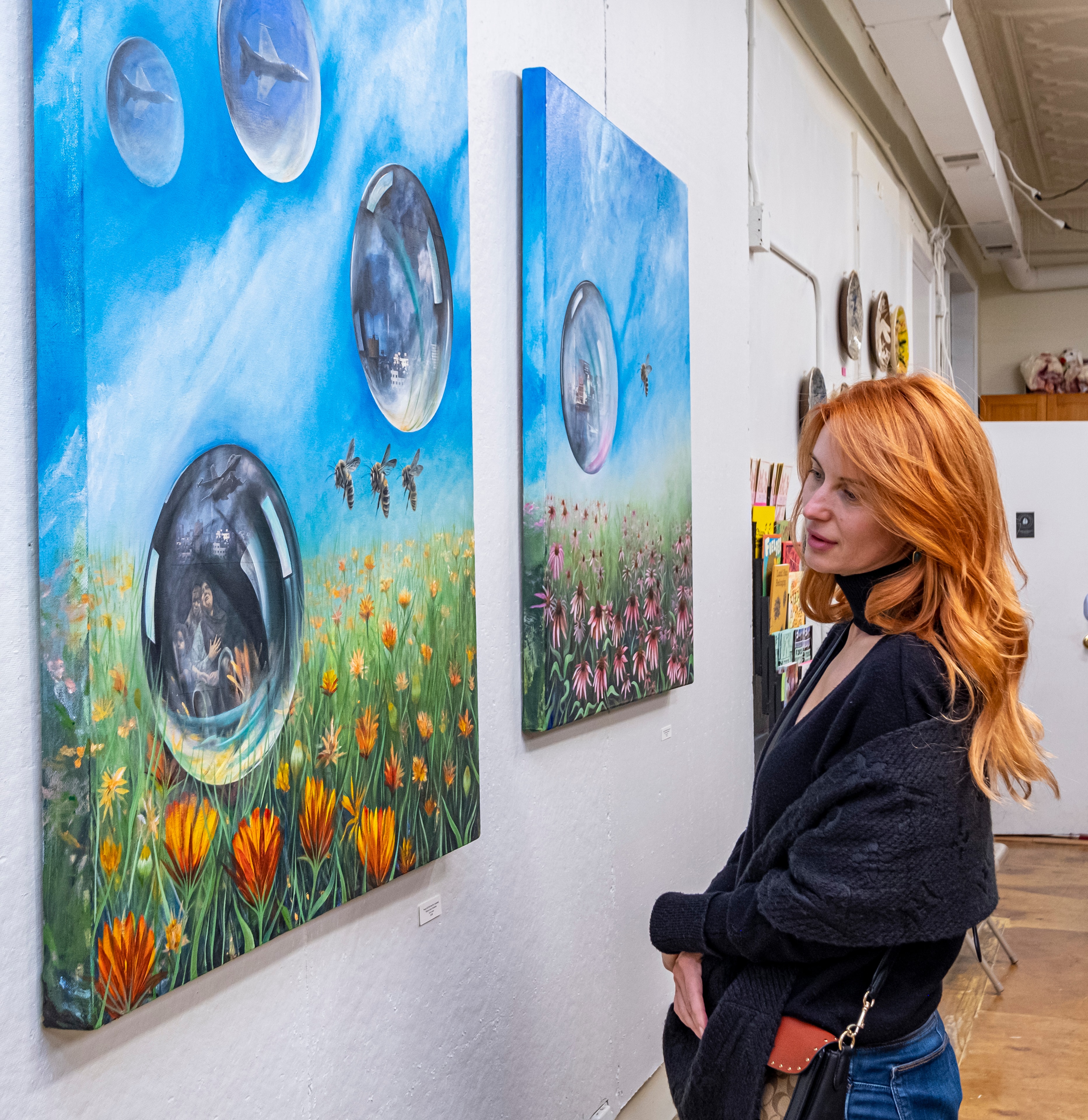 Echo of Resistance — A guest pauses before Ricardo's Healing Plants paintings at Hoof Print Chicago. The large-scale canvases — spheres reflecting bees, wildflowers, and the quiet persistence of the natural world against industrial violence — fill the gallery wall. A still moment of contemplation in the middle of the exhibition. Photography by Fugi Almanza. by Ricardo Santos Hernández